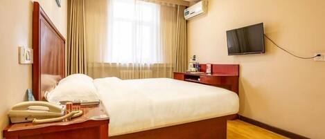 Une chambre d’hôtel avec un grand lit, des tables de chevet en bois, une télévision et une fenêtre avec des rideaux.