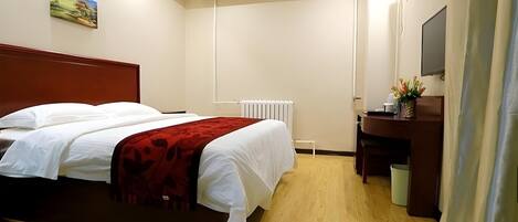 Une chambre d’hôtel avec un lit double, un bureau avec une chaise, un radiateur et un téléviseur fixé au mur.