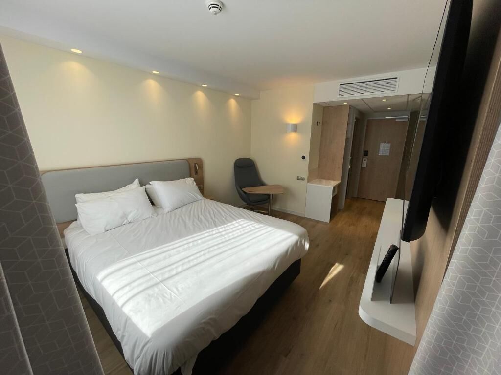 A hotel room with a bed, a chair, a desk, and a television.