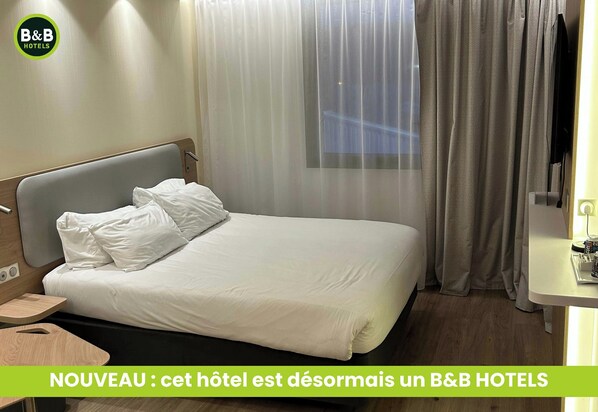A hotel room with a bed, curtains, a bedside table, and a television. - B&B Hotel Deauville-touques (Touques)
