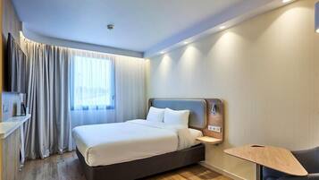 A modern hotel room with a bed, bedside table, and a small desk.