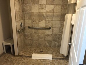 A shower area with a glass door, a handrail, a white towel, and a small stool. - Rodeway Inn and Suites Walhalla SC (Walhalla)