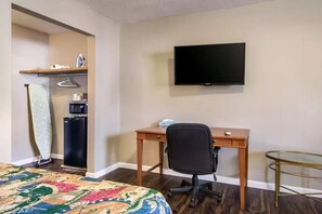 A hotel room with a bed, a desk with a chair, a television, a small refrigerator, and a glass table. - Rodeway Inn and Suites Walhalla SC (Walhalla)