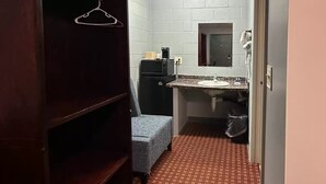 A small, compact bathroom with a sink, mirror, and a compact toilet. There is a small bench and a heater on the wall. - Rodeway Inn and Suites Walhalla SC (Walhalla)