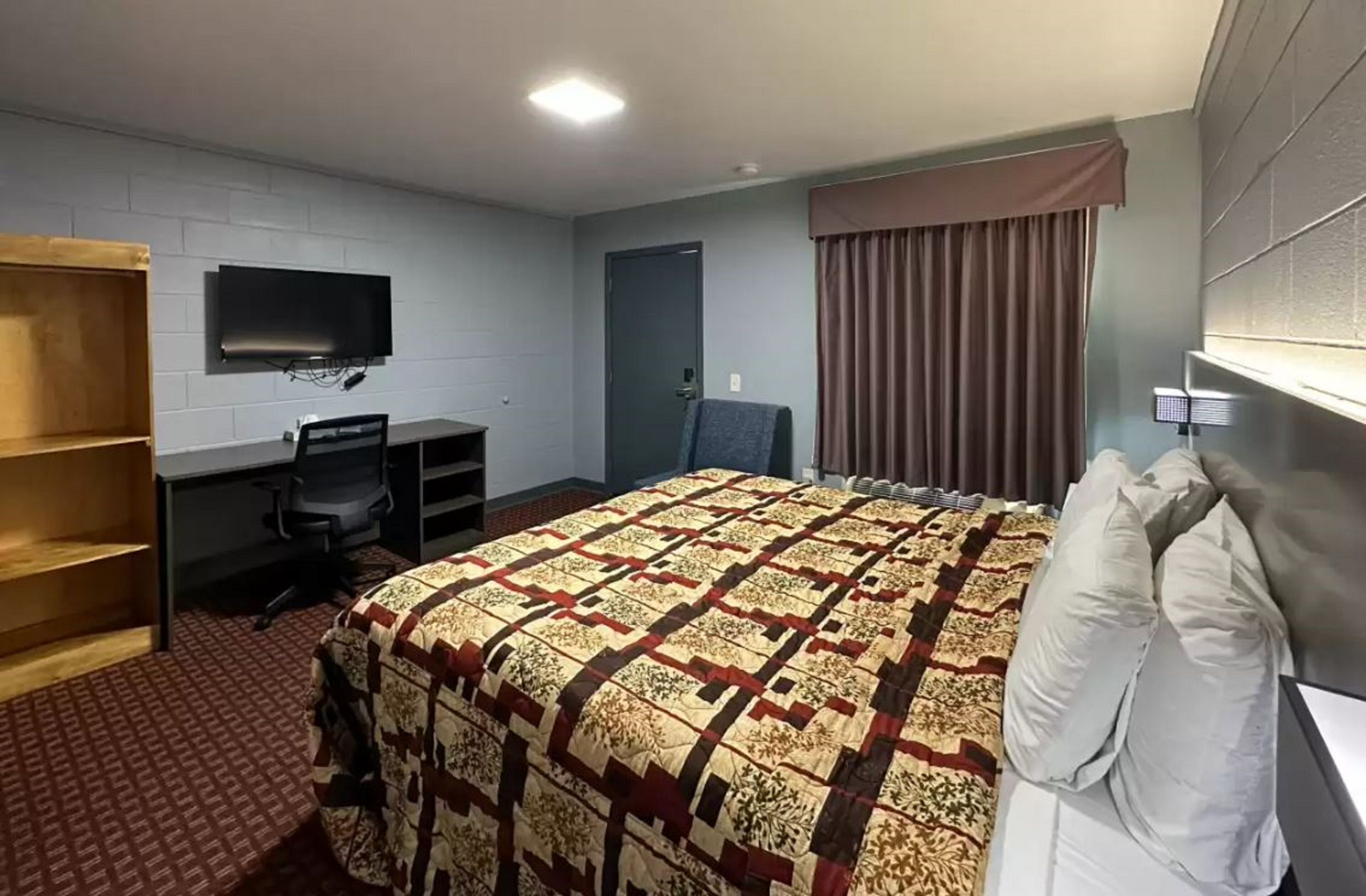 A hotel room with a bed, a desk, a chair, a TV mounted on the wall, and a door.