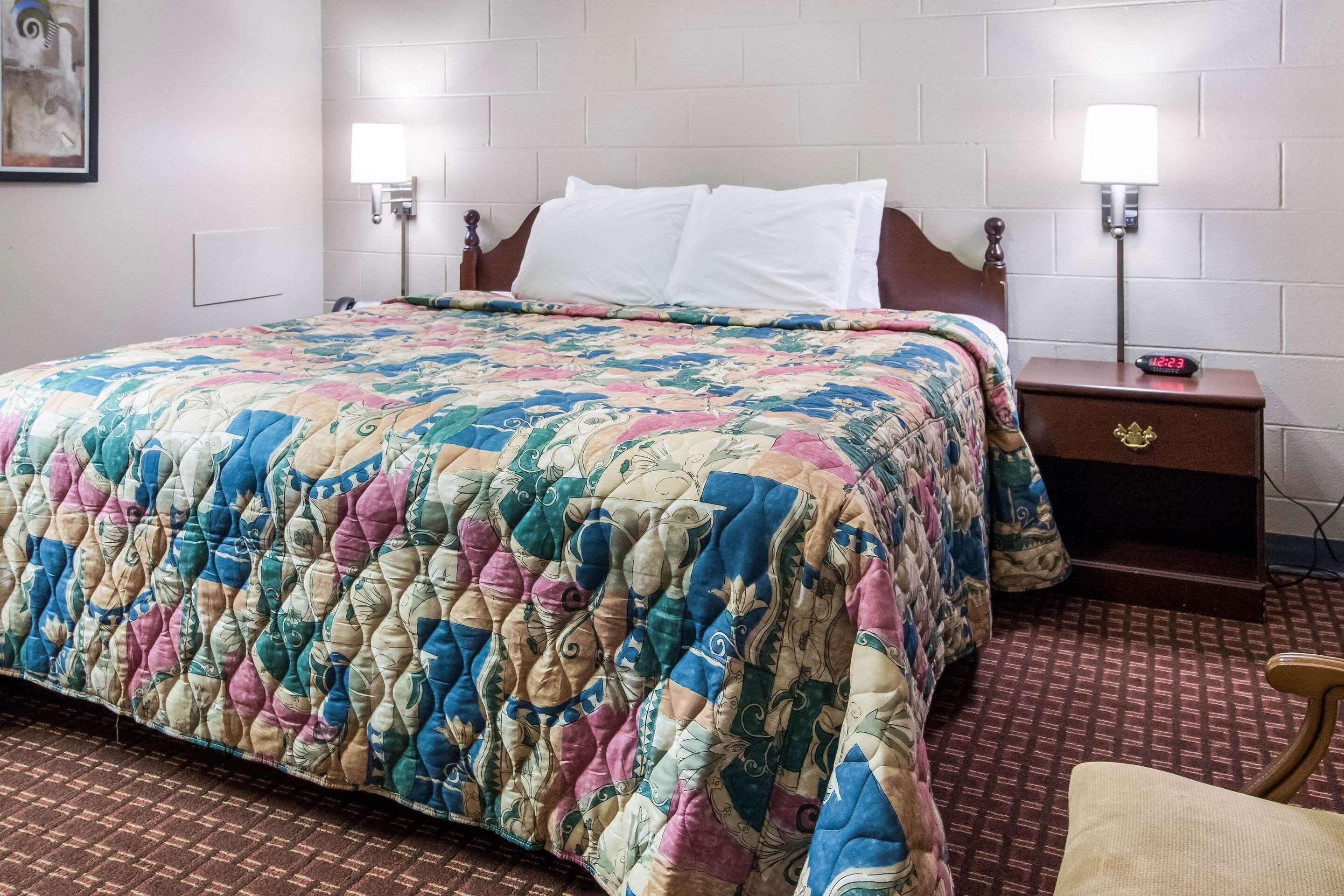Una habitación de hotel con una cama, dos lámparas de noche, una mesita de noche y una silla.