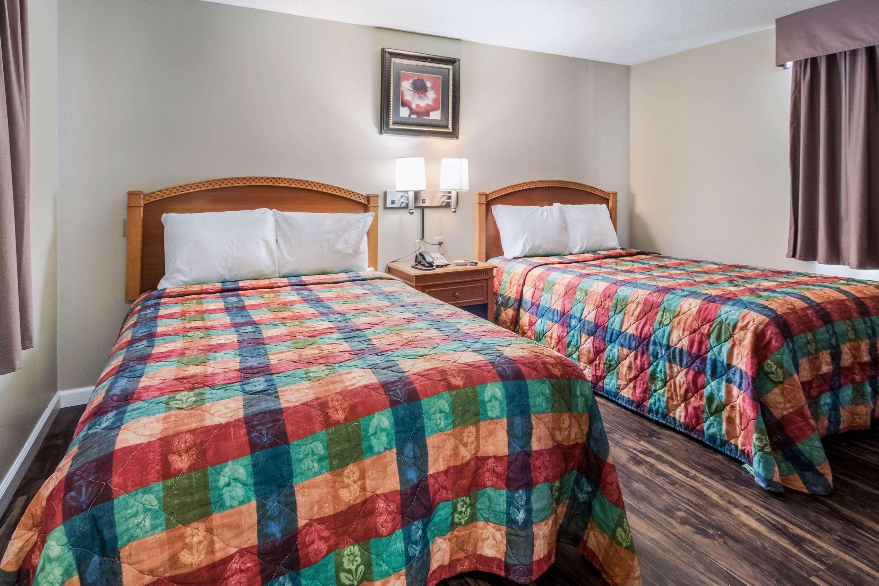 Een hotelkamer met twee bedden, elk voorzien van een kleurrijk quilt, een nachtkastje met een lamp, en een lijst met een foto aan de muur.