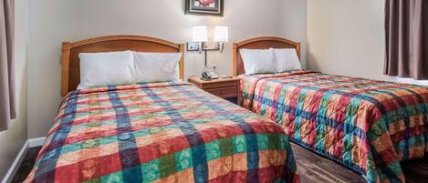 Een hotelkamer met twee bedden, elk voorzien van een kleurrijk quilt, een nachtkastje met een lamp, en een lijst met een foto aan de muur.