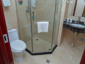 A glass-enclosed shower stall with a white towel hanging on the door handle, a toilet, and a sink with toiletries. - Greentree Inn Tangshan Ring Road South Ring and Fuxing Road Express Hotel (Tangshan)