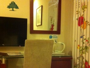 Une chambre d’hôtel équipée d’un téléviseur à écran plat, d’un tableau encadré, d’un miroir, de rideaux à motifs floraux et d’une machine à café posée sur une table.