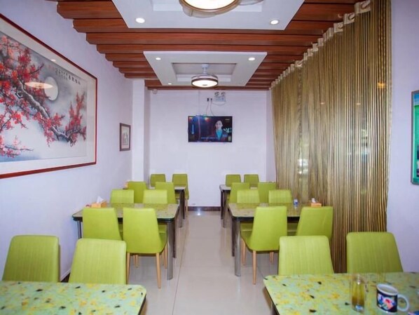 Une salle de conférence avec des chaises et des tables vertes, un tableau au mur et un écran de télévision.