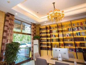 Un hall d’hôtel avec une grande bibliothèque, un lustre et un bureau équipé d’un ordinateur.