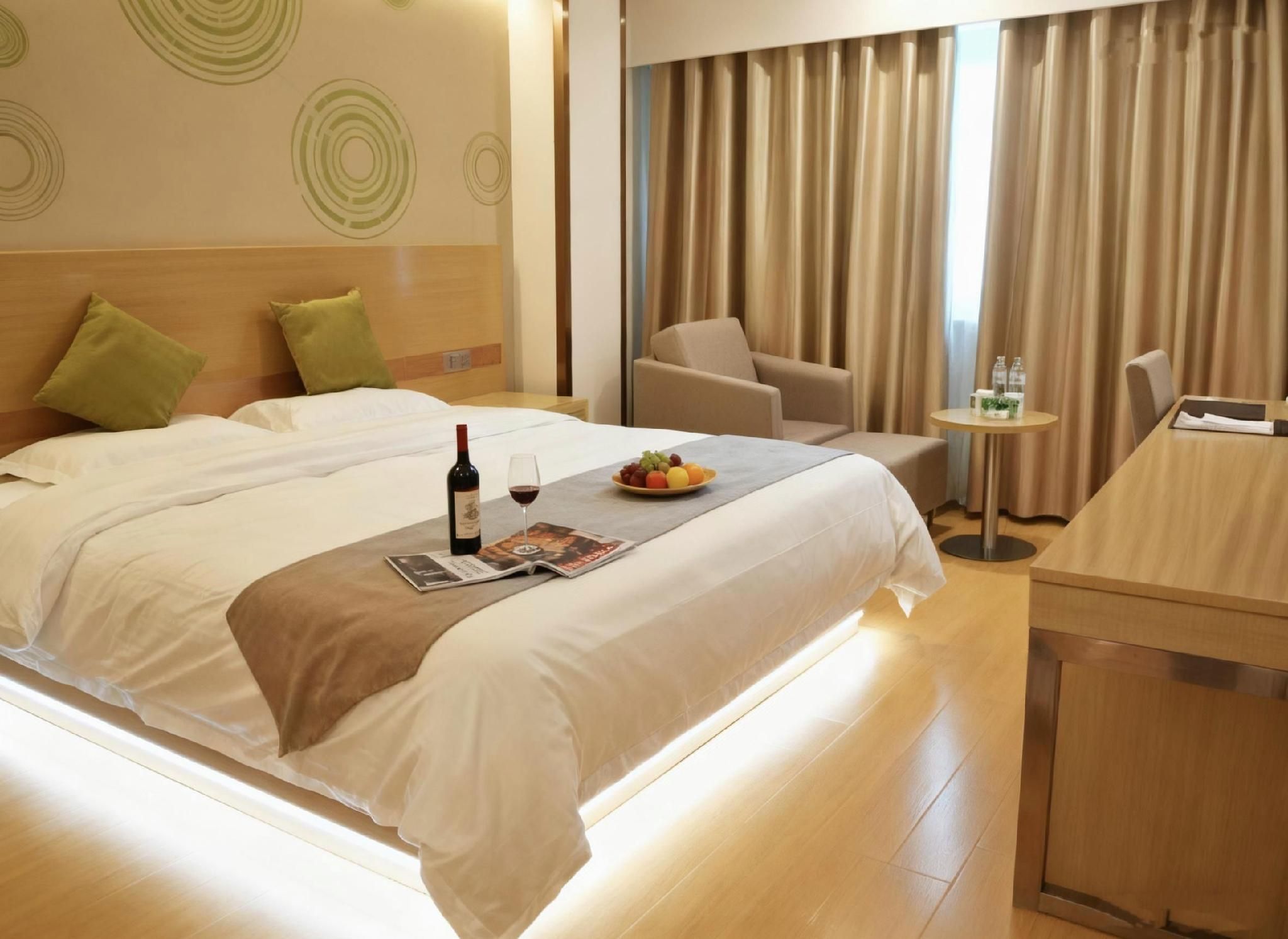 A hotel room with a bed, a small table with a bottle of wine and fruit, a chair, and a desk with a chair.