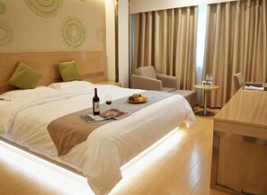 Habitación de hotel con cama, una mesita con botella de vino y fruta, una silla y un escritorio con su propio asiento.
