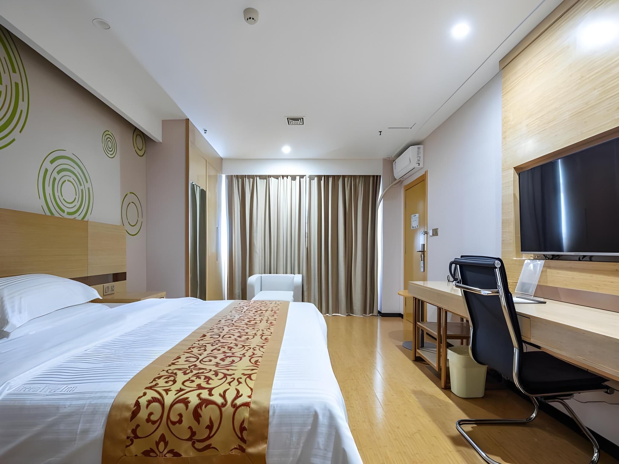Ein Hotelzimmer mit einem Bett, einem Schreibtisch, einem Sessel, einem Fernseher und einem Vorhang.