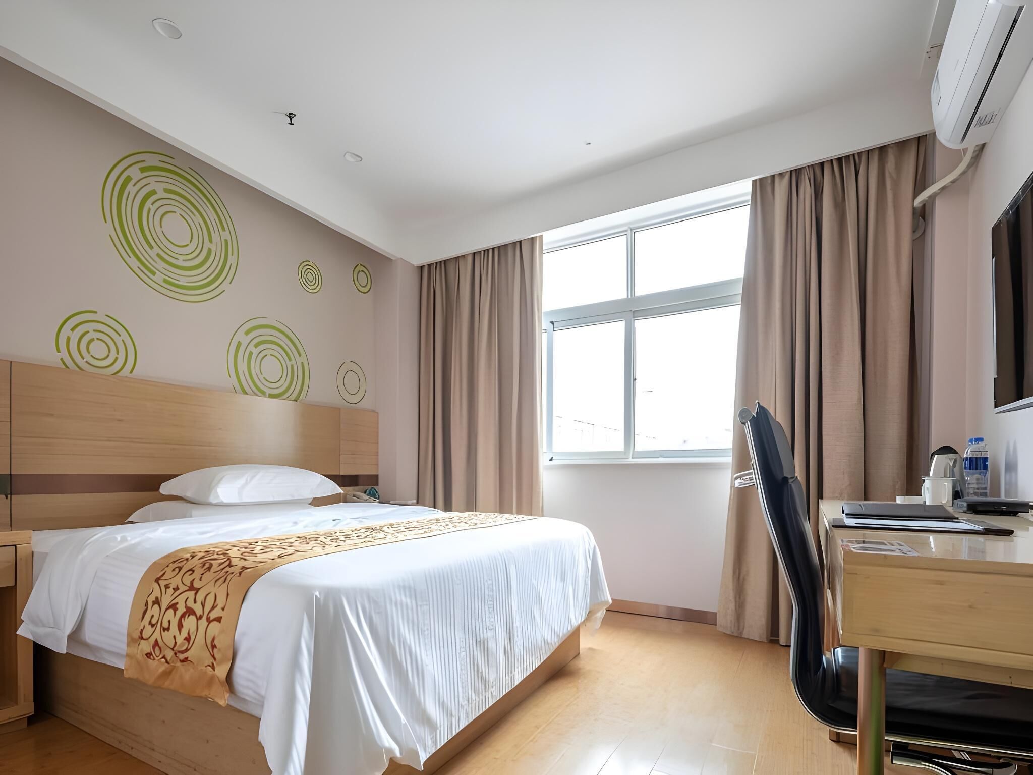 A hotel room with a bed, a desk, a chair, a TV, and a window with curtains.