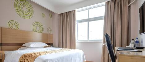 A hotel room with a bed, a desk, a chair, a TV, and a window with curtains.