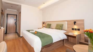 Una habitación de hotel con cama, mesita de noche, silla y una pequeña mesa con un jarrón de flores.