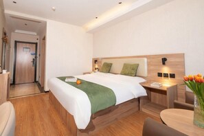 A hotel room with a bed, bedside table, chair, and a small table with a vase of flowers. - Greentree Inn Hefei Economic Development Zone Convention and Exhibition Center Business Hotel (Hefei)