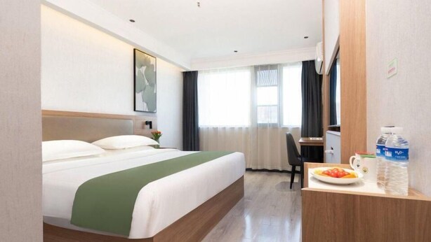 Habitación de hotel con cama, escritorio con silla, ventana con cortinas y dispensador de agua sobre el escritorio.