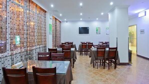 Un comedor con varias mesas y sillas, una pared con diseño decorativo, un televisor de pantalla plana montado y un suelo de baldosas.