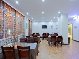 Un comedor con varias mesas y sillas, una pared con diseño decorativo, un televisor de pantalla plana montado y un suelo de baldosas.