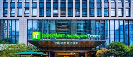 Un hôtel Holiday Inn Express doté d’une façade moderne, de grandes fenêtres et d’un espace extérieur aménagé pour s’asseoir.