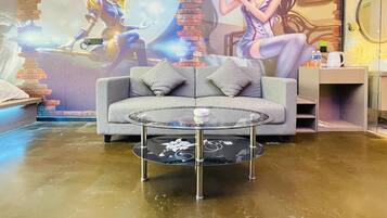 A modern living room with a grey sofa, a glass coffee table, and a mural on the wall.