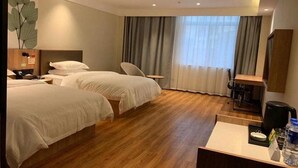 Ett hotellrum med två sängar, ett skrivbord, en stol, en kaffebryggare och ett stort fönster med gardiner.
