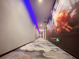 Un pasillo de hotel con alfombra estampada, una tira iluminada en azul y un cartel grande en la pared derecha.