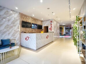 A hotel reception area with a marble reception desk, a sofa, and a television screen. - Shell Shanghai Baoshan District Songbin Road Subway Station Hotel (Shanghai)