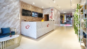 Un hall d’accueil d’hôtel avec un comptoir de réception en marbre, un téléviseur fixé au mur et un comptoir de réception orné d’un logo.