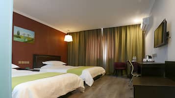 Habitación de hotel con dos camas, un escritorio, una silla, un cuadro en la pared y un ventanal con cortinas.