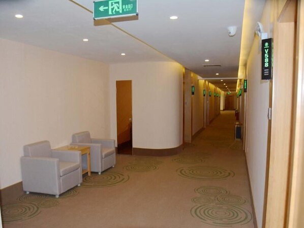 Een hotelgang met een zithoek, een groen vluchtroutebord en een bord met het kamernummer V588.