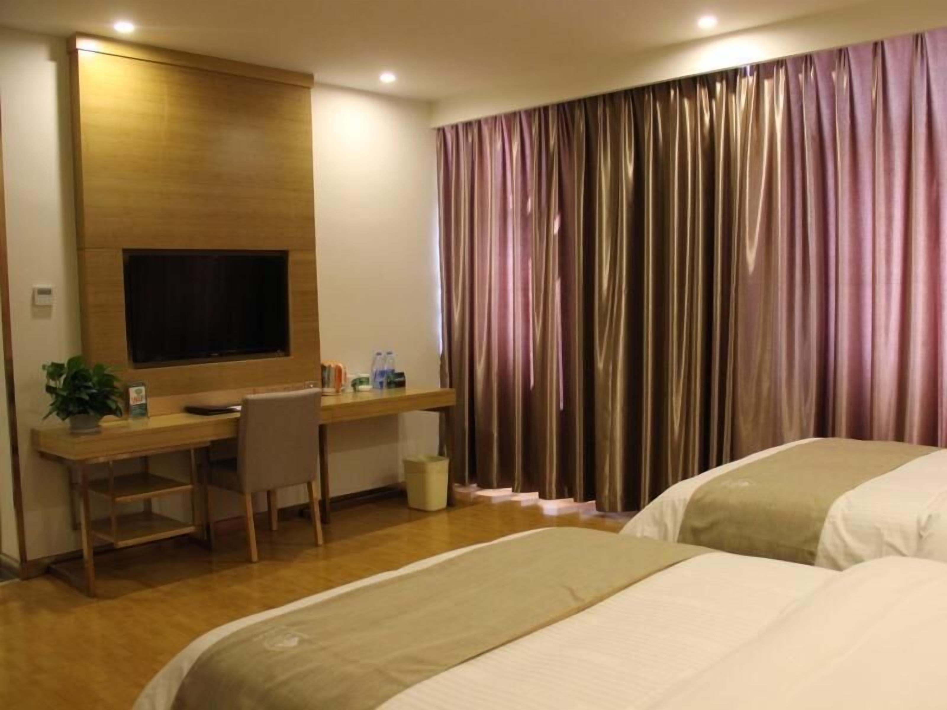 Una habitación de hotel con un escritorio de madera, un televisor, una cama y una cortina.