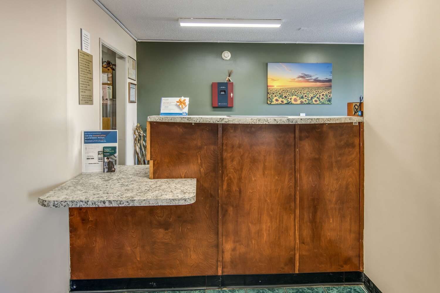 Un comptoir d’accueil avec un revêtement en bois, une horloge au mur et un tableau encadré représentant un coucher de soleil.