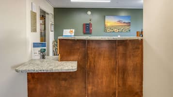 Un comptoir d’accueil avec un revêtement en bois, une horloge au mur et un tableau encadré représentant un coucher de soleil.