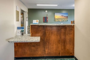 A reception desk with a wooden finish, a clock on the wall, and a framed picture of a sunset.