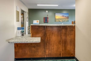 A reception desk with a wooden finish, a clock on the wall, and a framed picture of a sunset. - Rodeway Inn & Suites Dublin, GA (East Dublin)