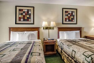 Habitación de hotel con dos camas, cada una con una colcha estampada, una mesita de noche con lámpara y un colcha enmarcada en la pared.