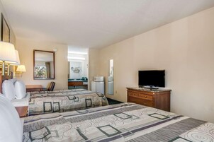 Habitación de hotel con dos camas, televisión, cómoda, espejo y ventana.