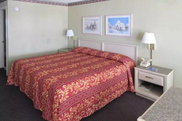 A hotel room with a large bed, two bedside tables with lamps, a small bedside table with a telephone, and two framed pictures on the wall. - Rodeway Inn San Juan (McAllen)