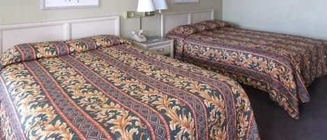 A hotel room with two beds, each with patterned bedding, a nightstand with a lamp, and framed artwork on the walls.