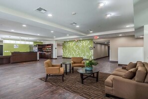 Vestíbulo de hotel con mostrador de recepción, zona de estar y un mural de plantas en la pared.