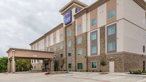 A multi-story hotel with a stone facade, a covered entrance, and a sign for Sleep at the top. - Sleep Inn and Suites College Station Area (College Station)