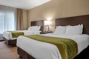 A hotel room with two beds, each with white linens and green throw blankets. There is a nightstand with a lamp and a phone. The room has a wooden headboard and beige walls. - Comfort Inn Connellsville Riverview (Connellsville)
