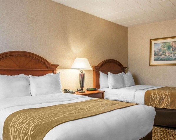 A hotel room with two beds, a nightstand with a lamp, a painting on the wall, and a brown throw blanket on one bed.