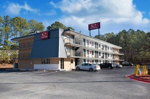 Un motel de varios pisos con estacionamiento, varios autos estacionados y un cielo despejado.