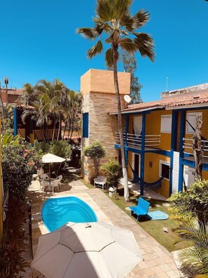 A pool area with a blue pool, white umbrellas, and palm trees. - Pousada Girassol (Ipojuca)