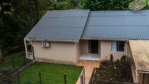 Una casa a due piani con tetto in lamiera ondulata, un piccolo portico e un cortile recintato con un giardino.